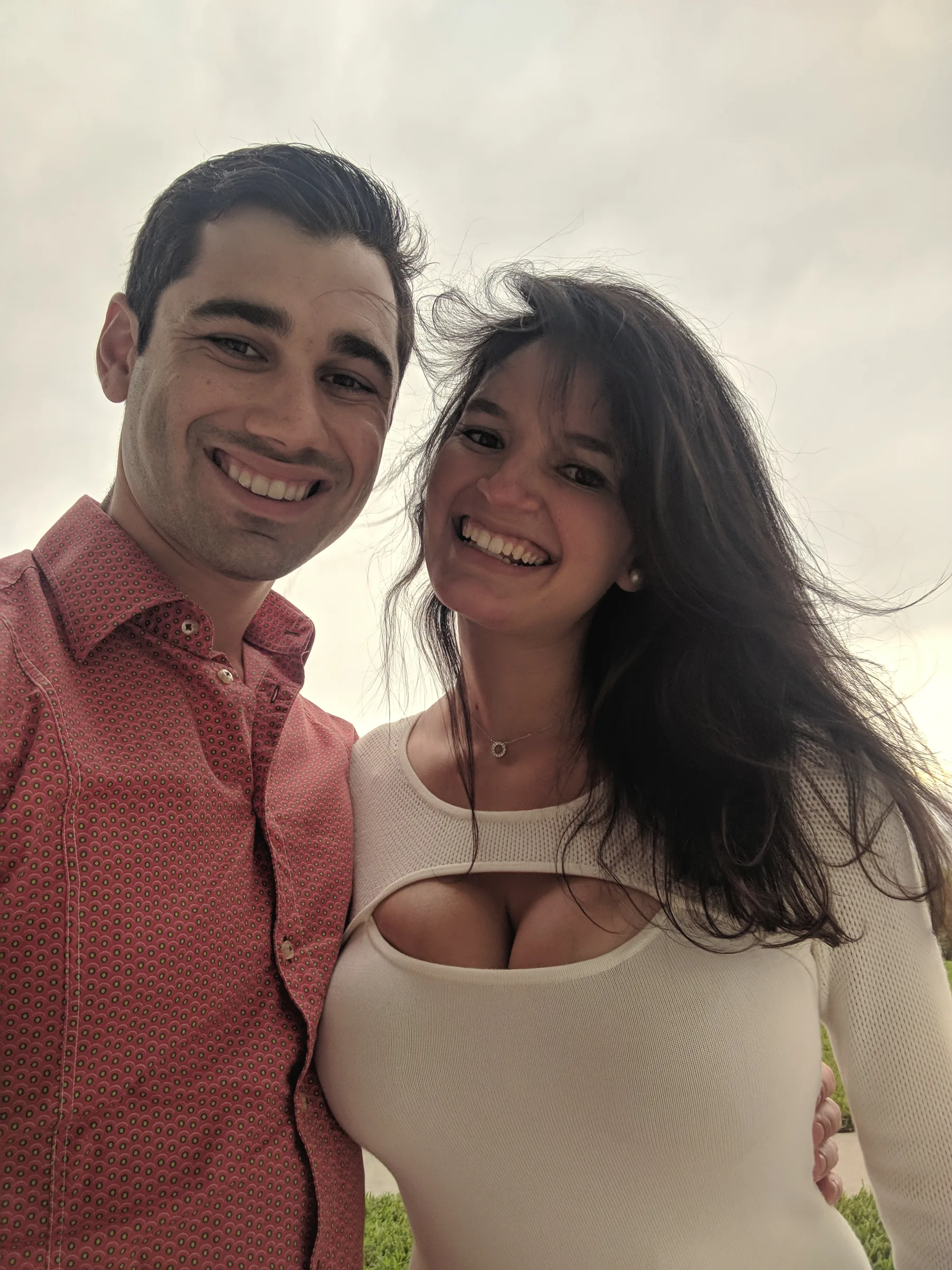 Carmela and Charlie smiling in a close selfie, her long hair blowing across her face