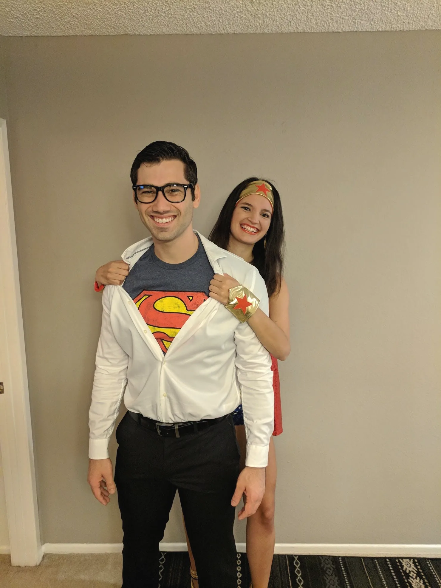 Charlie opening his white shirt to show a Superman logo while Carmela, in a red and blue costume, peeks over his shoulder