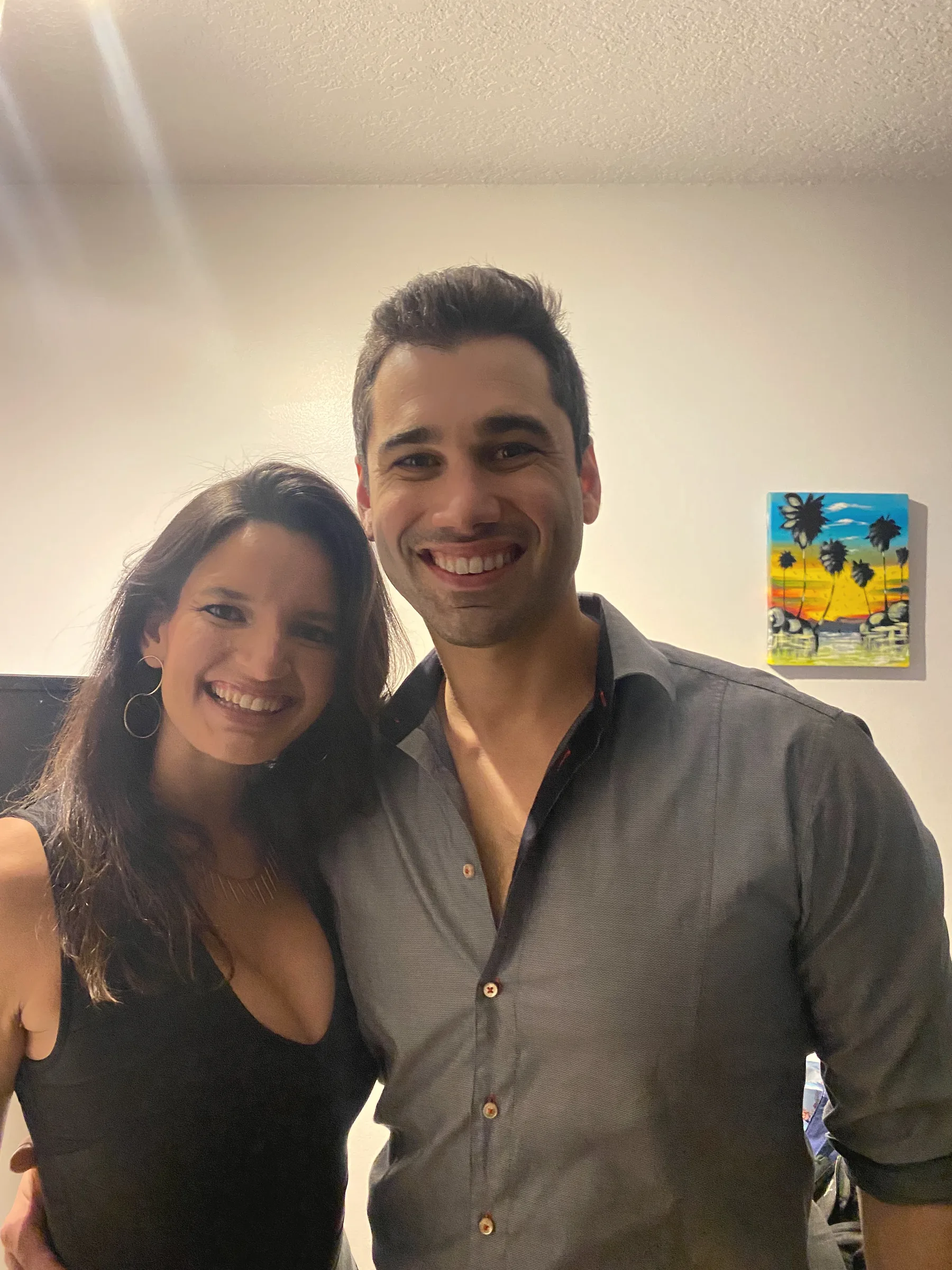 Carmela and Charlie smiling together in a room with a colourful painting on the wall