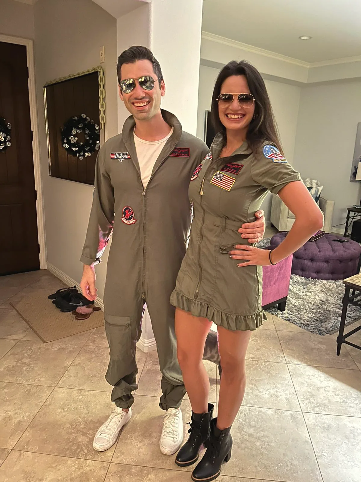 Charlie and Carmela in olive flight suits, aviator sunglasses and boots, standing in a bright hallway