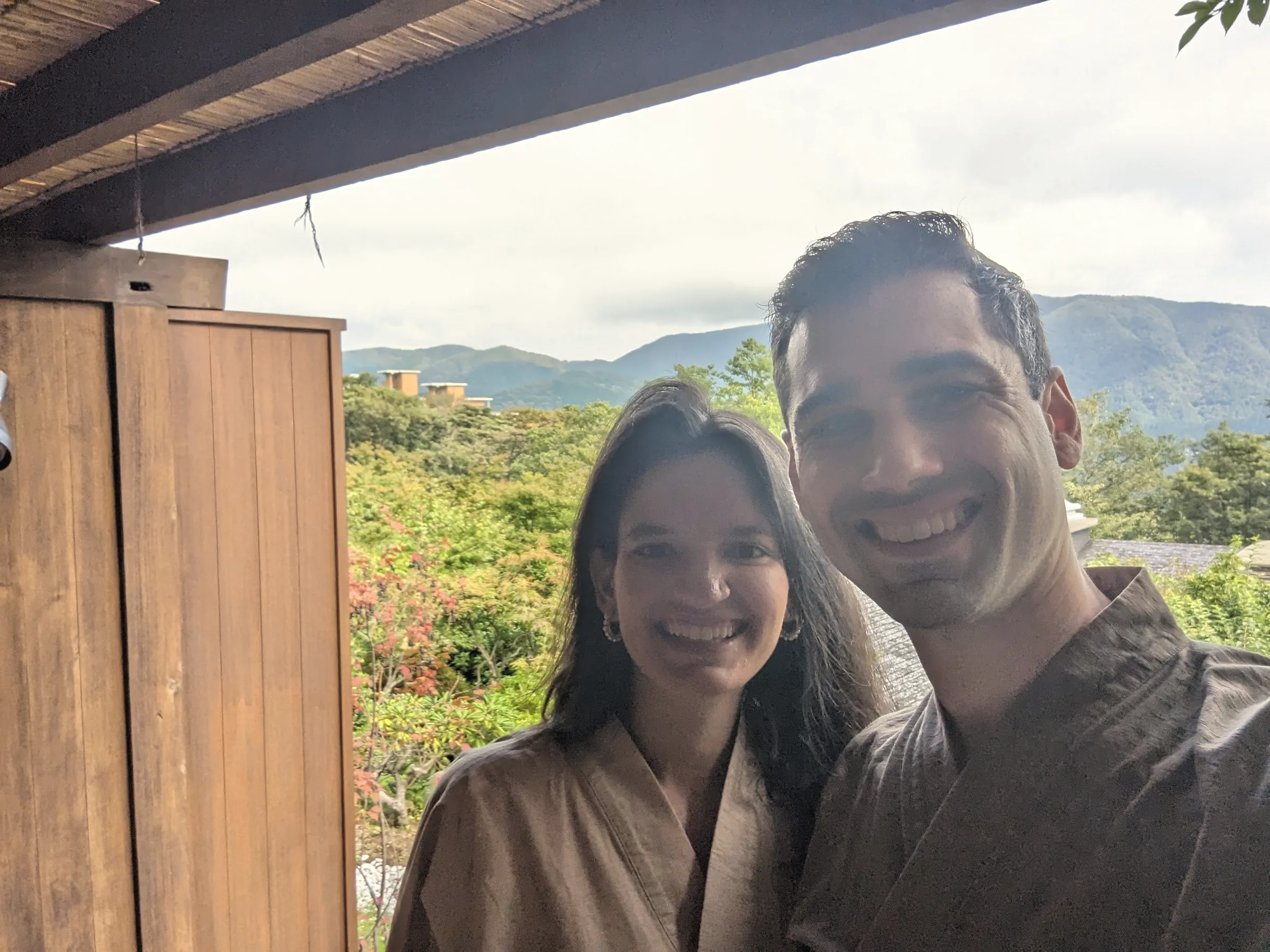 Carmela and Charlie smiling in robes, green hills and a wooden door behind them