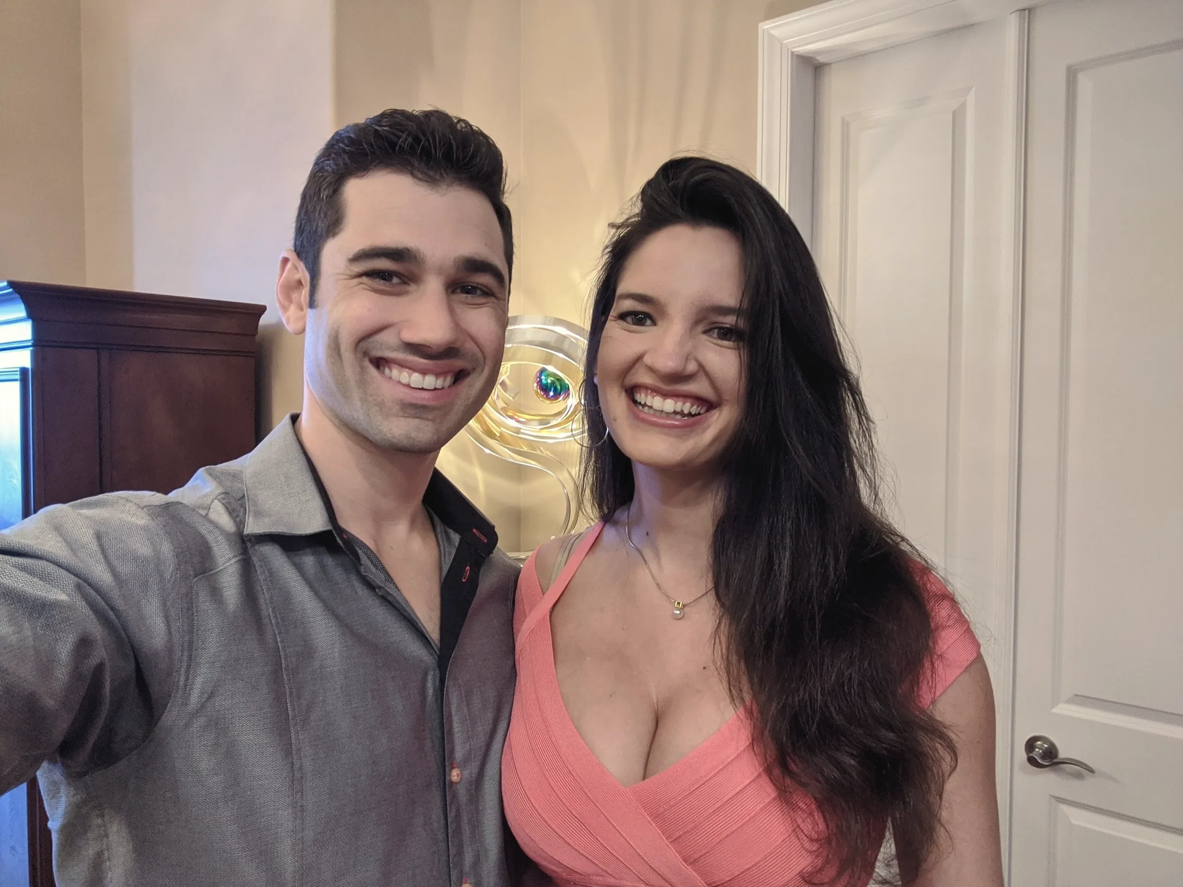 Charlie and Carmela in a smiling selfie next to a white door in a warmly lit room