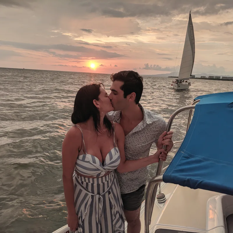 Carmela and Charlie kissing on a boat at sunset, a sailboat on the horizon