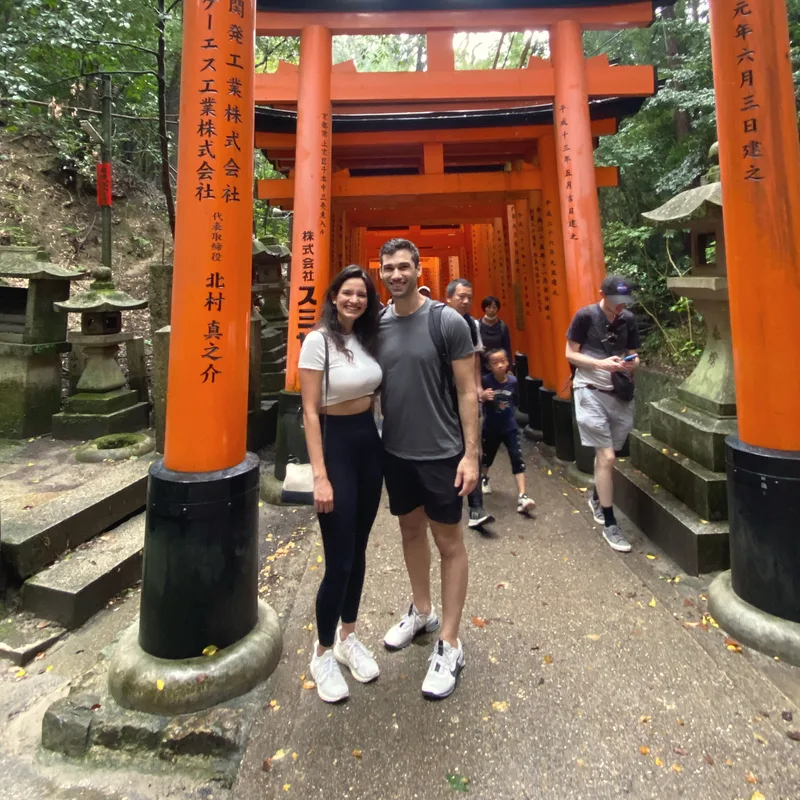 Carmela and Charlie standing in the red-orange torii gates of a Japanese shrine path
