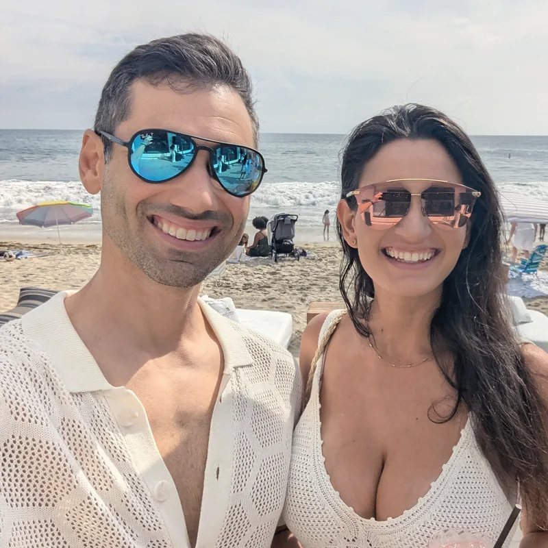 Carmela and Charlie in sunglasses smiling in a selfie on a sunny beach