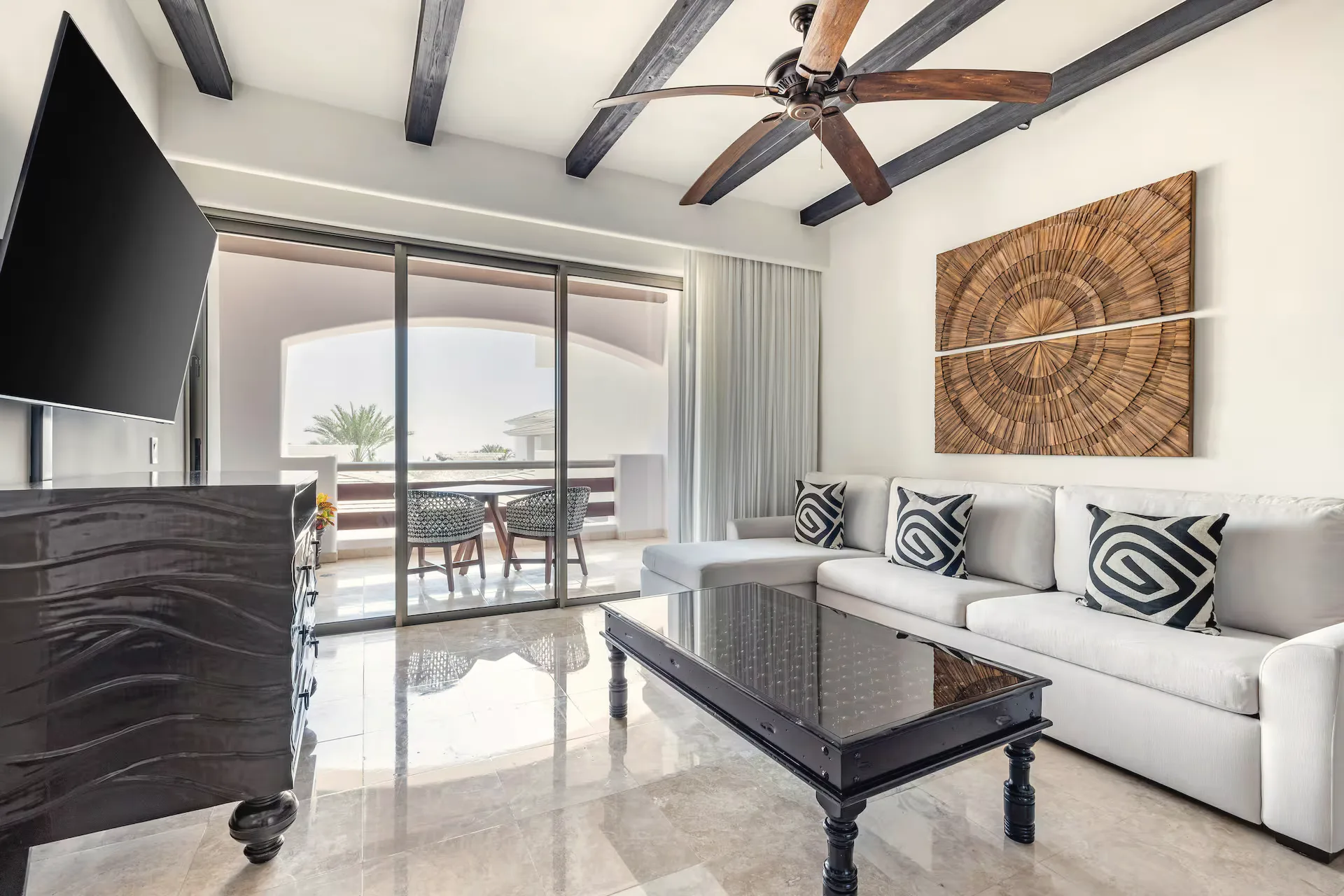 Living room with a white sofa, patterned cushions, a dark coffee table, a carved wood wall panel and sliding glass doors to a balcony.
