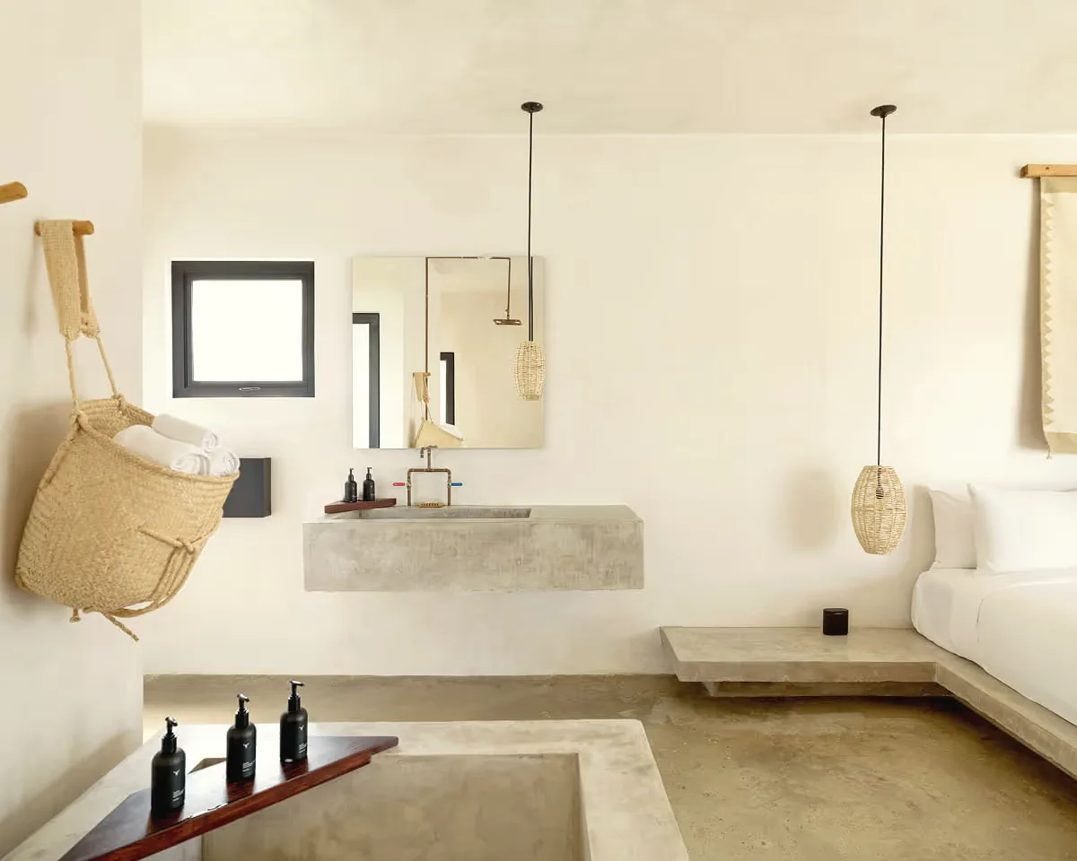 Wall-mounted concrete basin and mirror beneath a hanging basket, with a sunken concrete tub in the foreground.