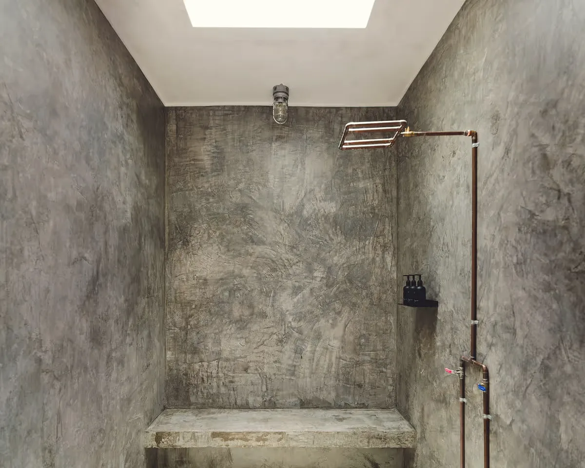 Shower with textured grey plaster walls, a copper shower pipe and a skylight.
