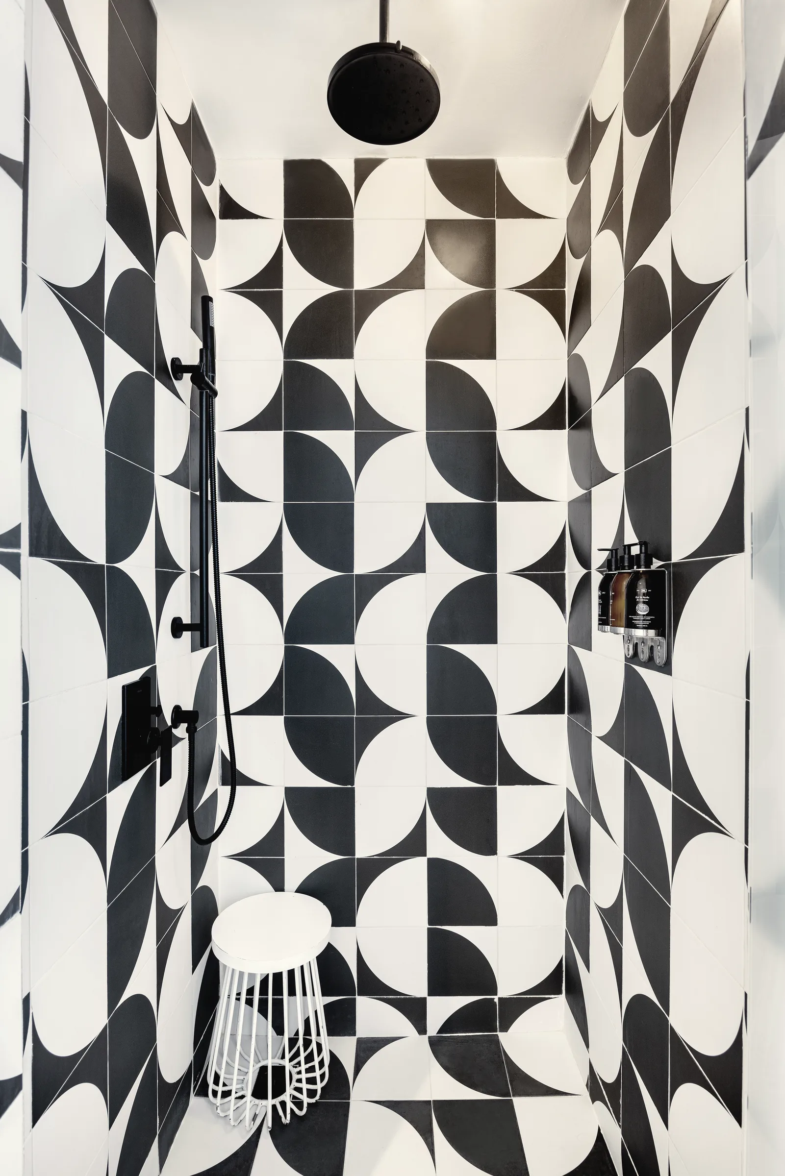 Walk-in shower with black-and-white geometric tile, a rain shower head and a small white stool.
