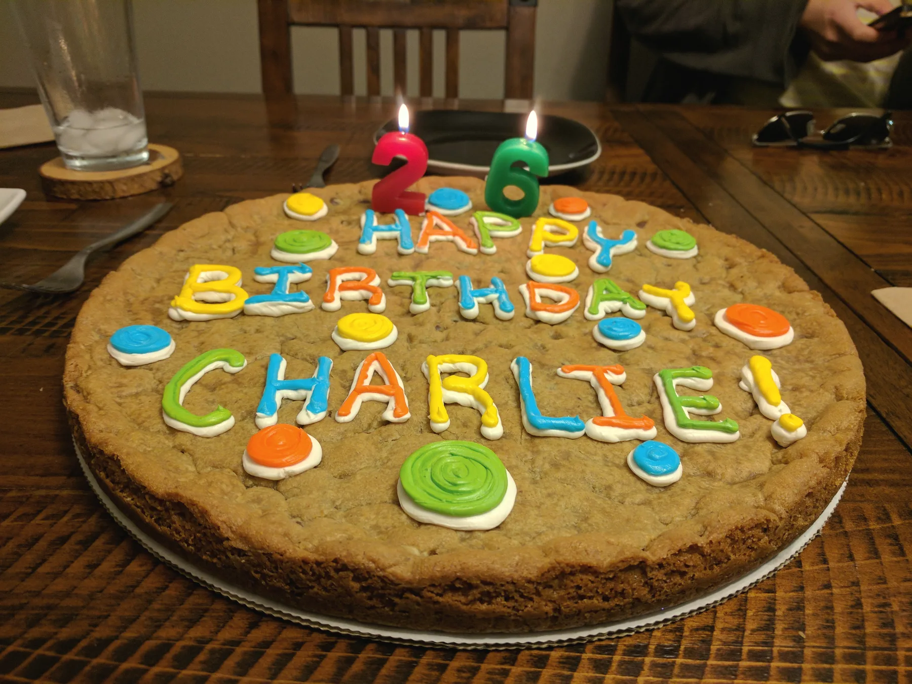A giant cookie cake iced with colourful letters reading Happy Birthday Charlie! and two lit candles shaped like a 2 and a 6