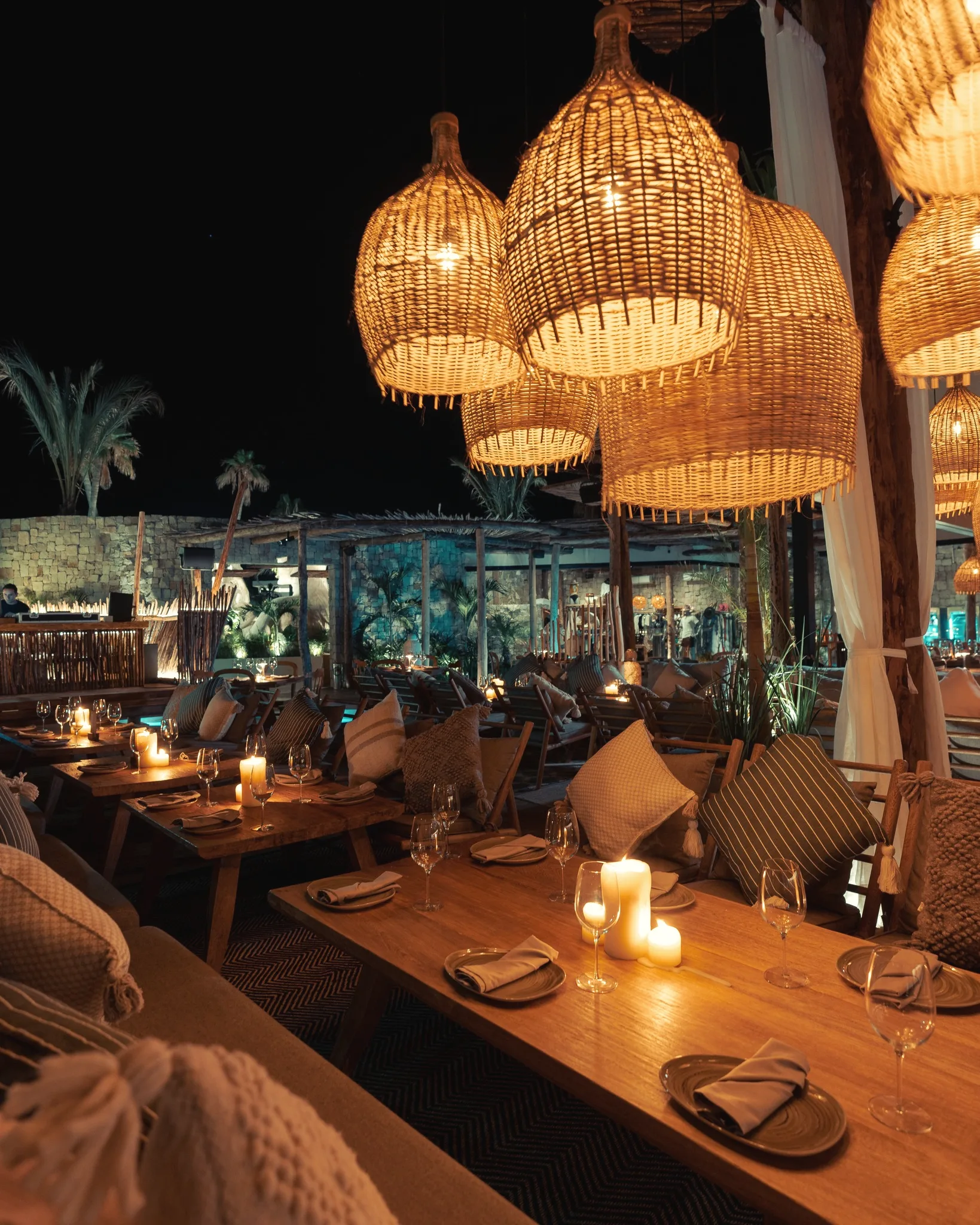 Woven pendant lamps glowing above candlelit tables at night