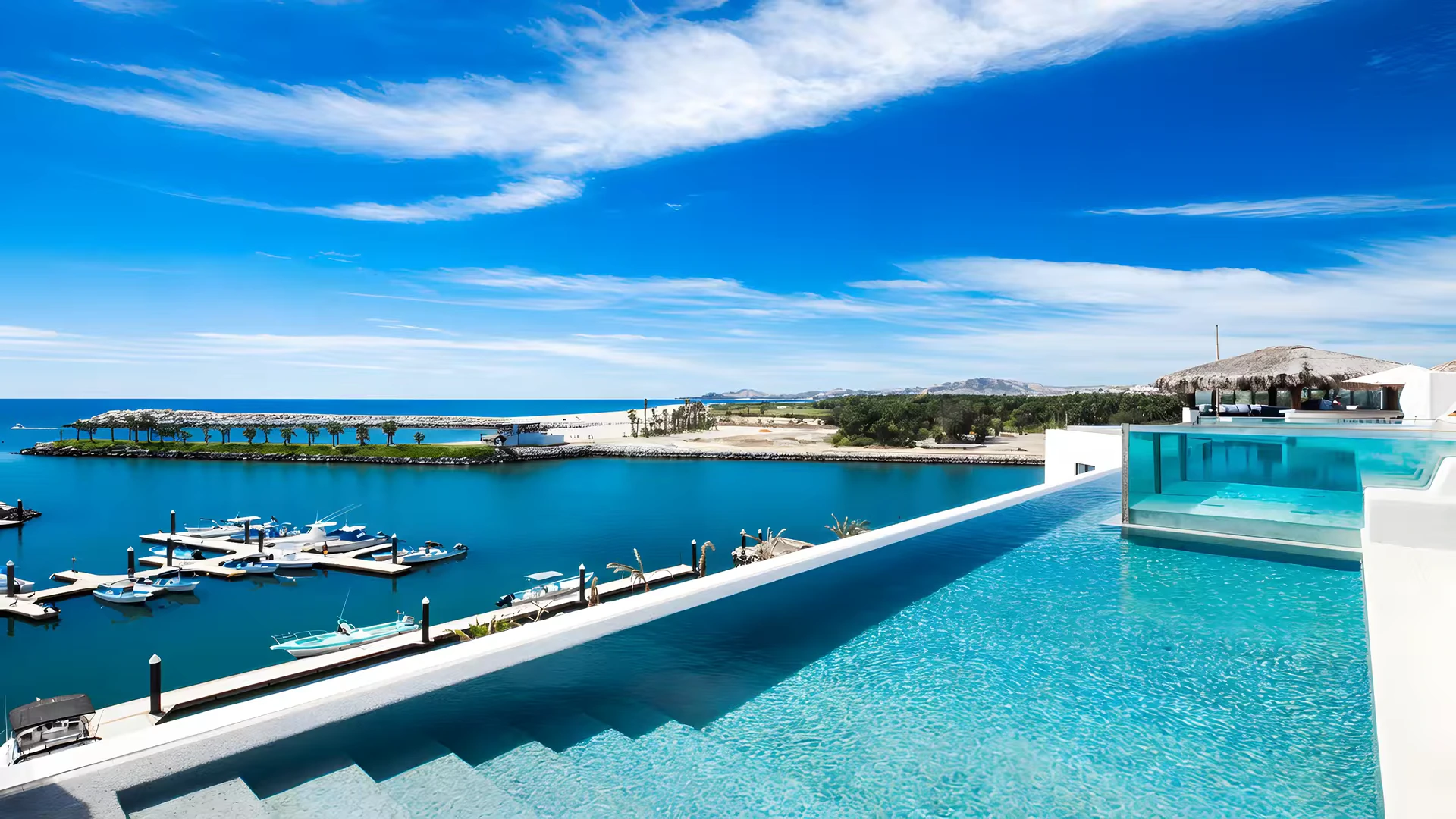 Infinity pool beside a marina with moored boats, a thatched palapa and the coast beyond