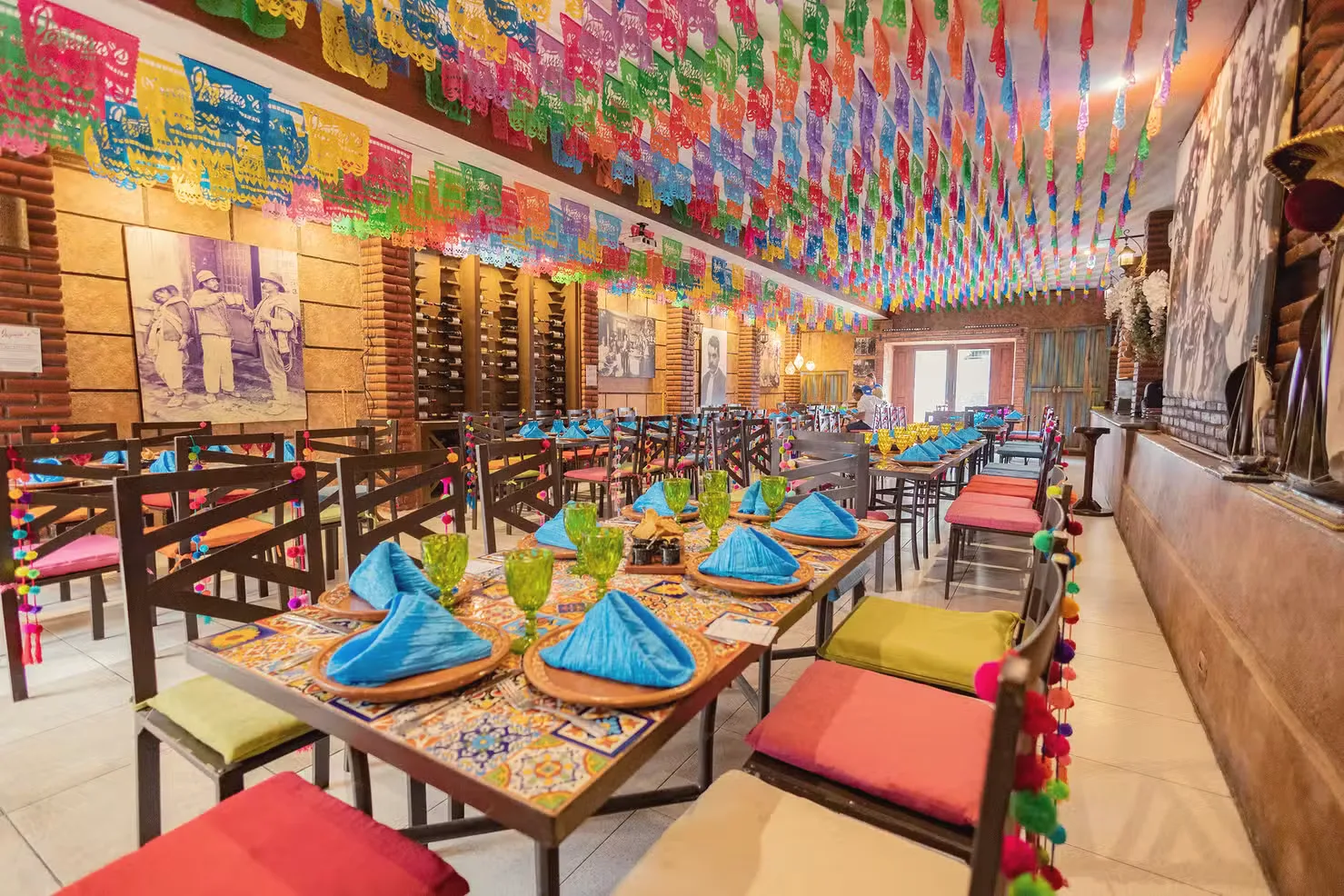 Long dining room hung with colourful papel picado, tables set with patterned tiles and turquoise napkins